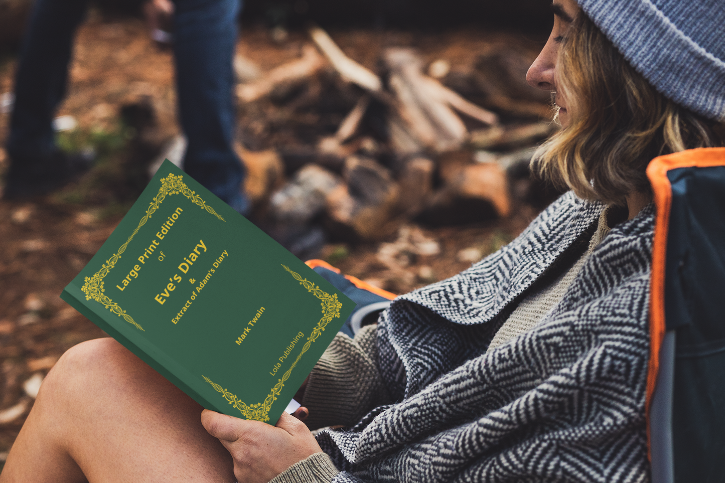 A woman reading a large print edition of Mark Twain's "Eve's Diary" at a camping site.